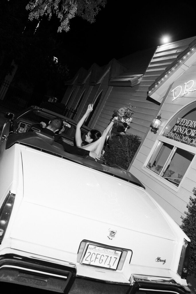 April Love Geary and Robin Thicke sitting in a classic white car for their Vegas elopement photos outside of A Special Memory Wedding Chapel