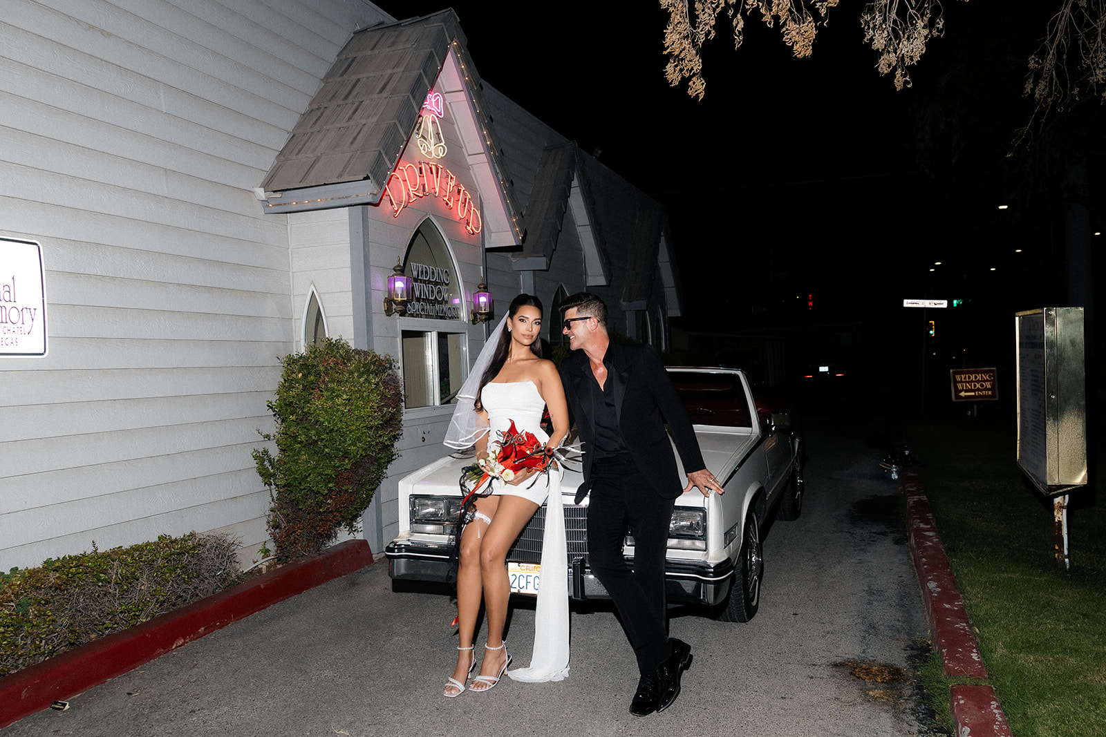 Robin Thicke and April Love Geary posing against a classic car in front of A Special Memory Wedding Chapel in Las Vegas