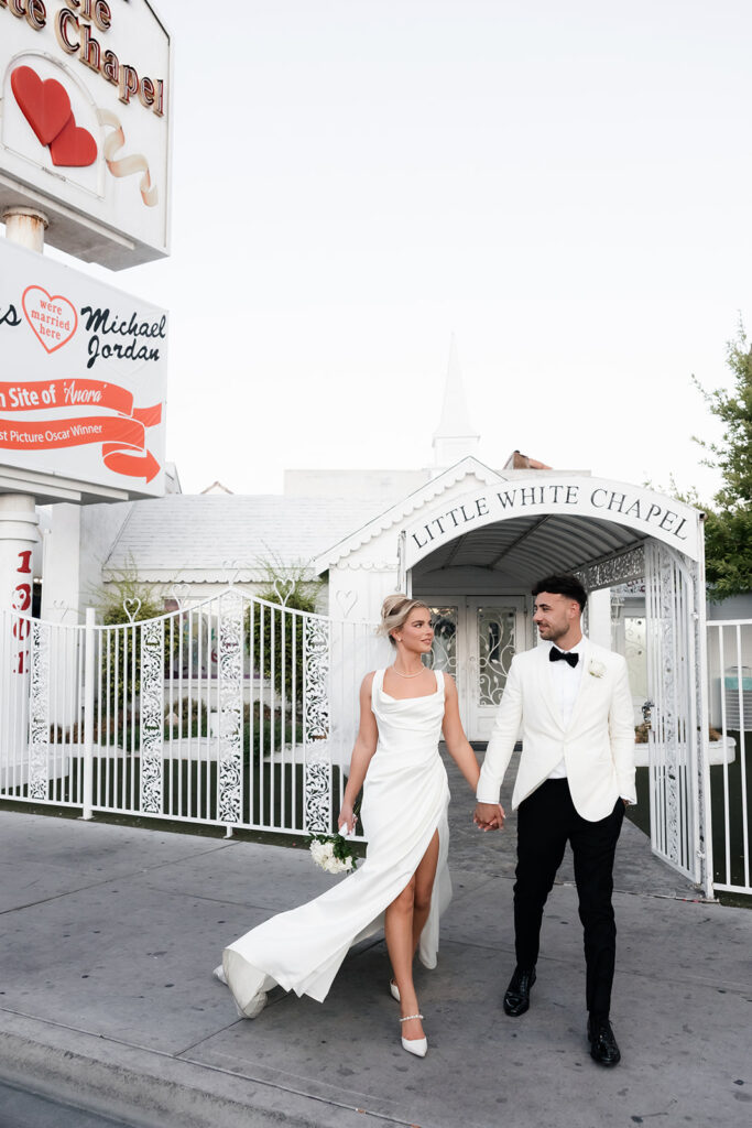 Bride and groom walking hand in hand in front of a Little White Chapel for their classy elopement in Vegas.