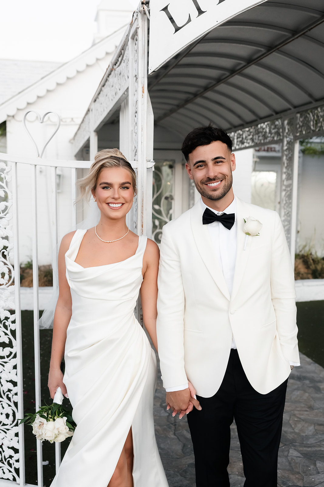 Close up shot of a bride and groom holding hands and smiling in front of Little White Chapel in Las Vegas.