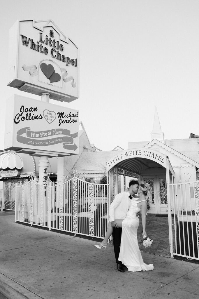 Black and white photo of a bride and groom posing in front of a Little White Chapel in Las Vegas.