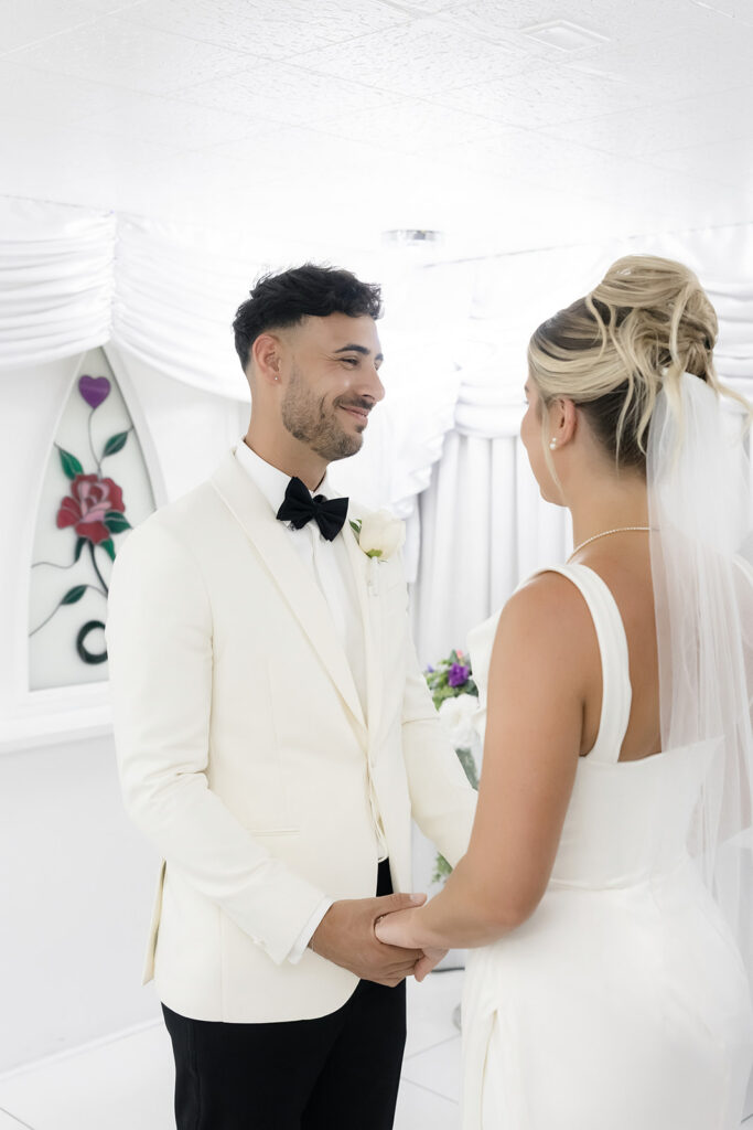 Bride and groom holding hands and smiling at each other during their Las Vegas elopement ceremony at Little White Chapel.