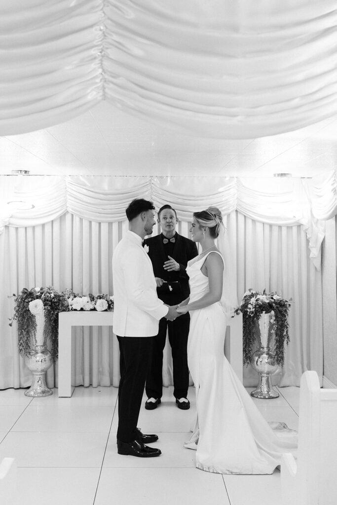 Black and white photo of a bride and  groom holding hands at the altar during their Little White Wedding Chapel ceremony in Las Vegas.