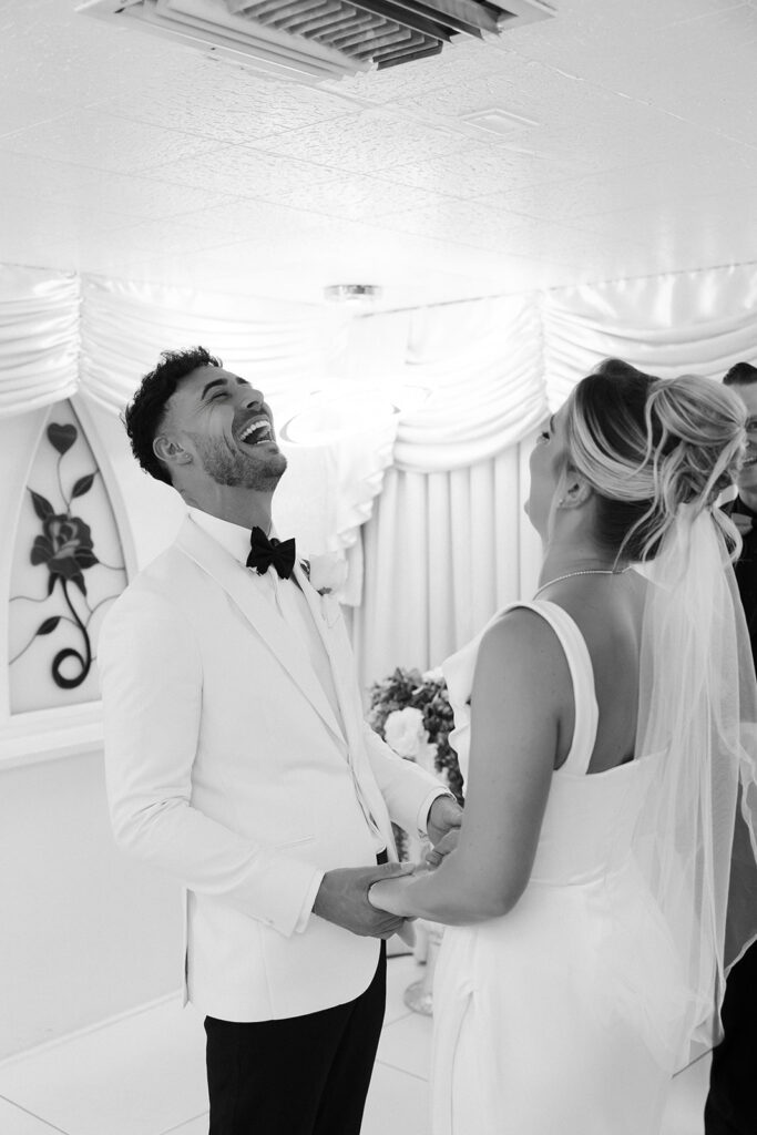 Black and white candid photo of a bride and groom laughing during their Las Vegas elopement ceremony at The Little White Wedding Chapel.