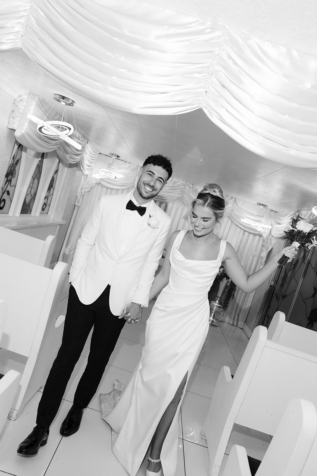 Black and white photo of a bride and groom walking back down the aisle after their classy elopement in Vegas at Little White Wedding Chapel.