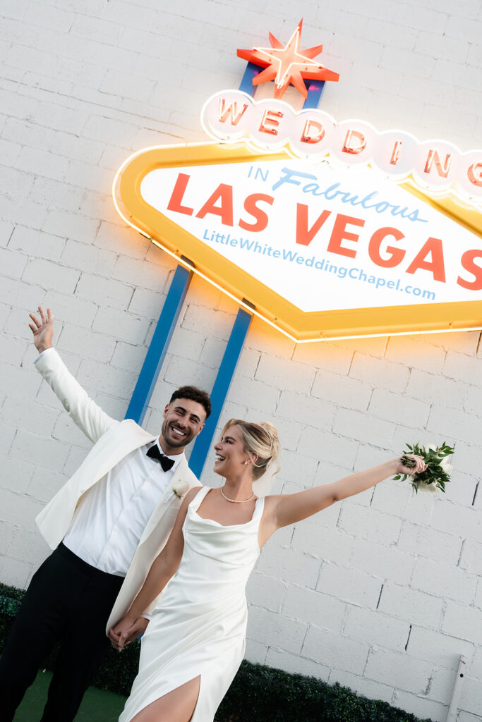Bride and groom posing in front a "Wedding in Fabulous Las Vegas" sign outside of The Little White Wedding Chapel.