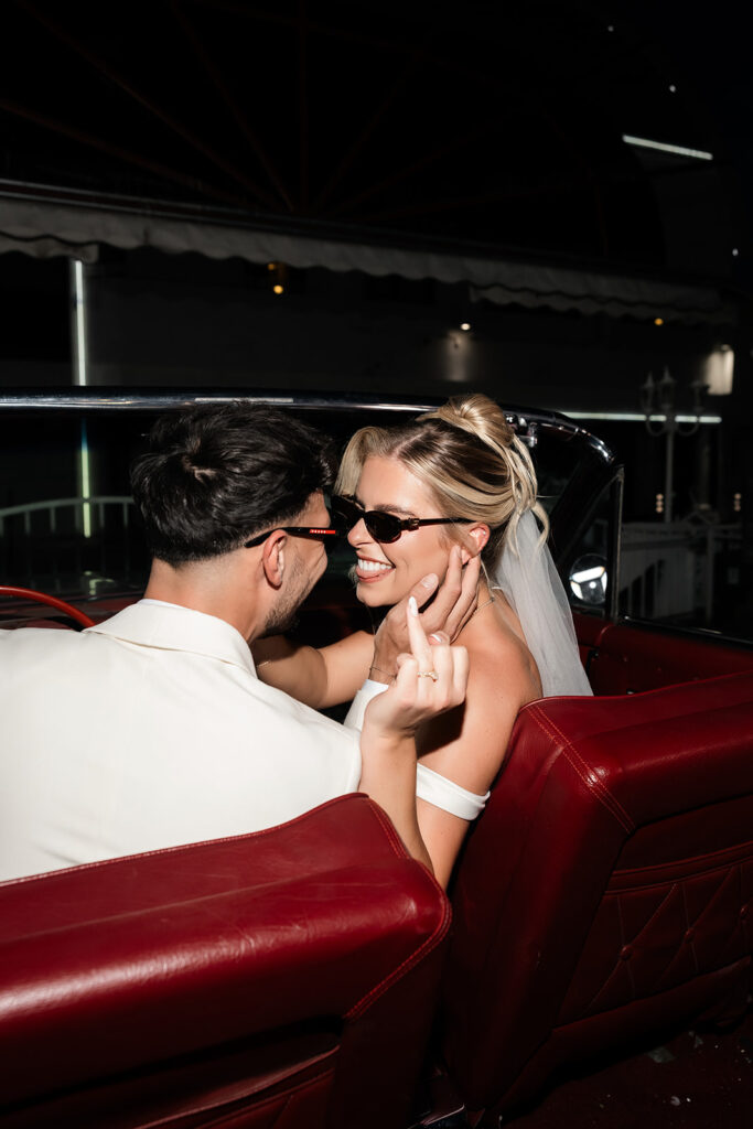 Bride and groom smiling at each other as they sit in the pink Cadillac at The Little White Wedding Chapel in Las Vegas.