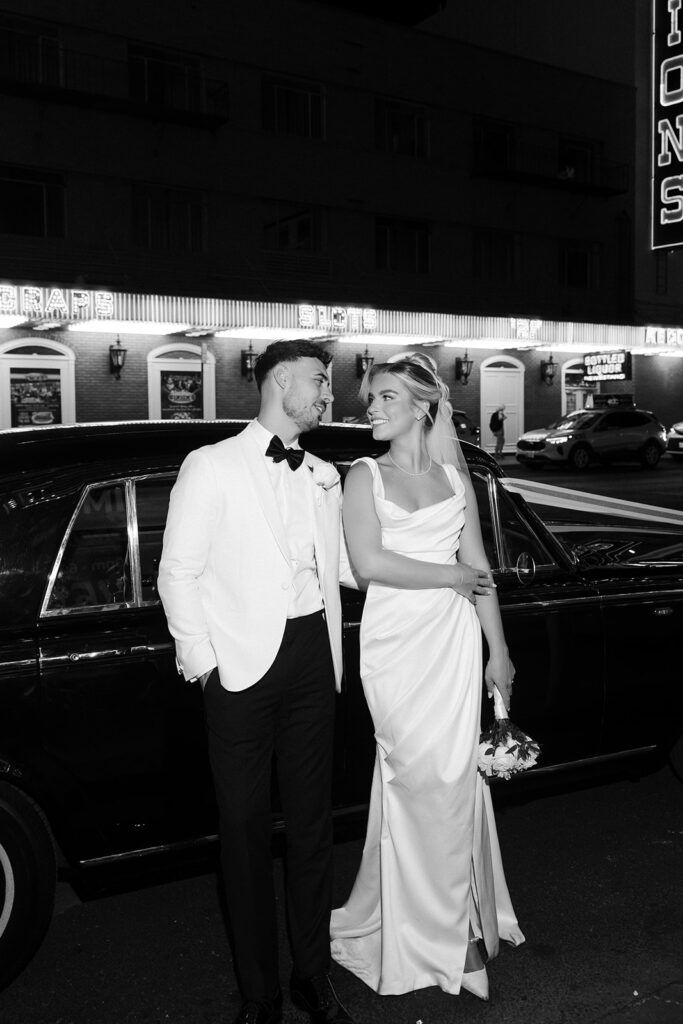 Bride and groom smiling at each other beside a vintage Rolls Royce on Fremont Street at night in Las Vegas.