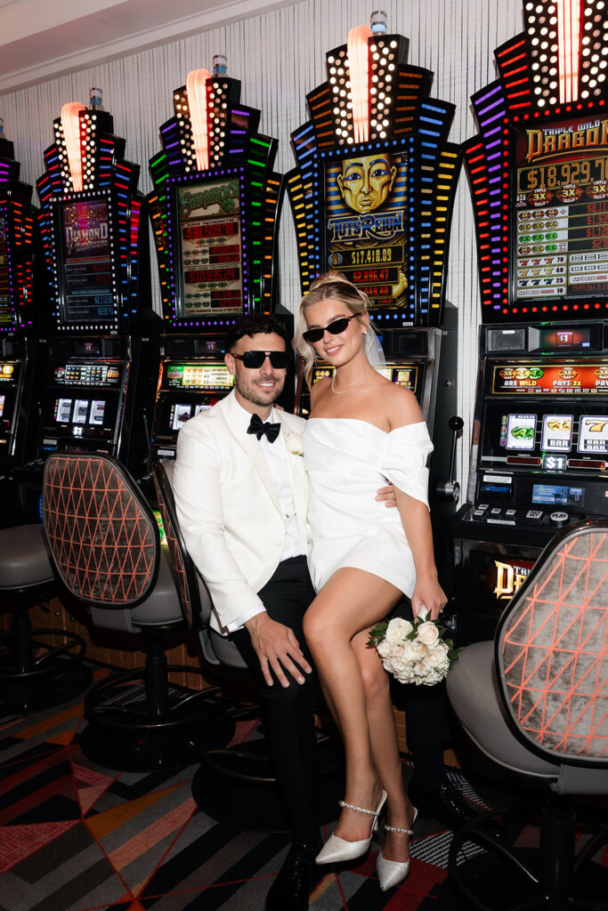 Bride and groom posing together inside a casino during their Las Vegas elopement with slot machines behind them.