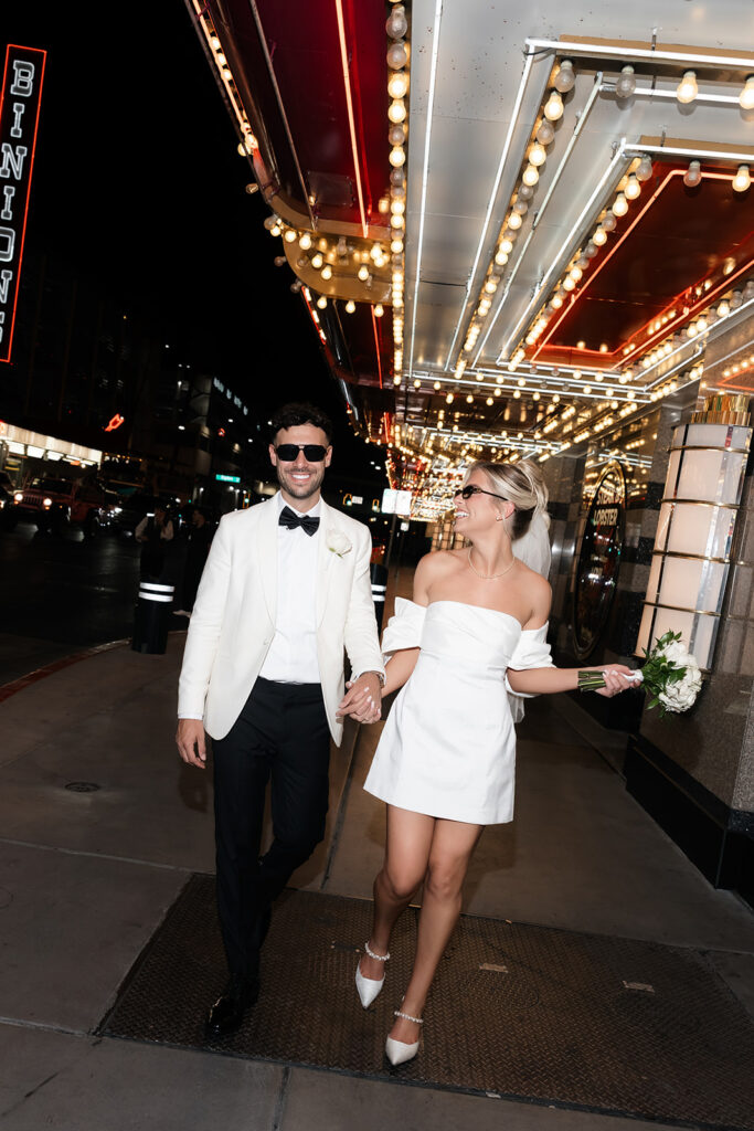 Bride and groom smiling at each other and walking down Fremont Street at night.