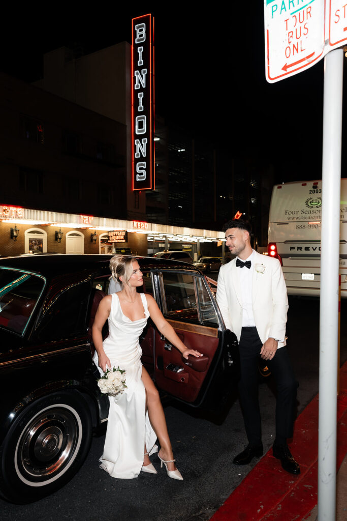 Bride and groom smiling at each other beside a vintage Rolls Royce on Fremont Street at night in Las Vegas.
