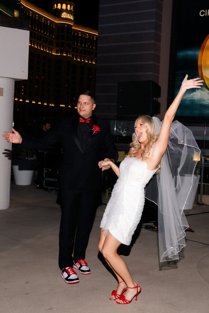 Bride raising her arms in celebration while dancing during a rooftop reception.