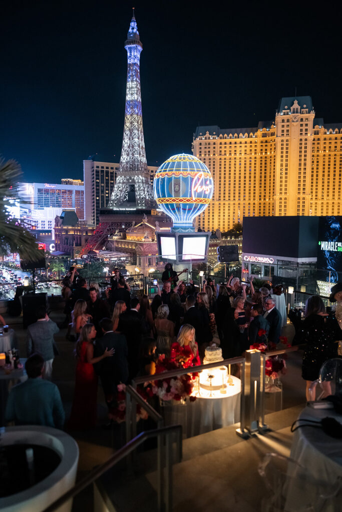 Wide view of a Cosmopolitan rooftop wedding reception with Paris Las Vegas and the Strip glowing in the background.