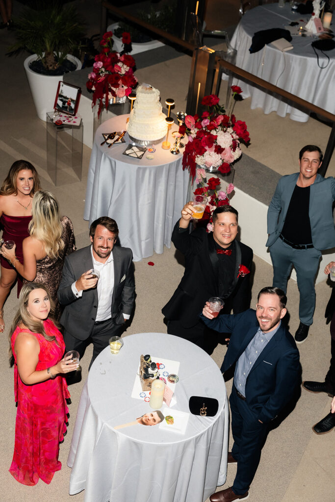 Overhead view of wedding guests raising drinks in celebration at a rooftop reception.