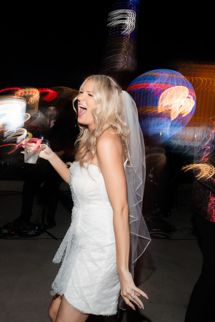 Bride laughing during her rooftop reception with a drink in hand.