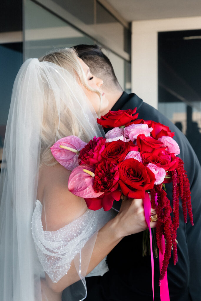 Bride holds a vibrant red and pink bouquet while standing behind the groom during their first look at a Cosmopolitan wedding in Las Vegas.