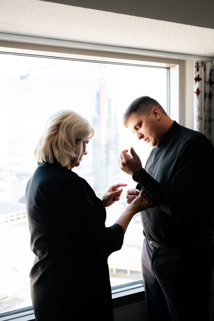 Groom has his cufflinks adjusted by a family member while getting ready in a hotel room for a Cosmopolitan wedding in Las Vegas.