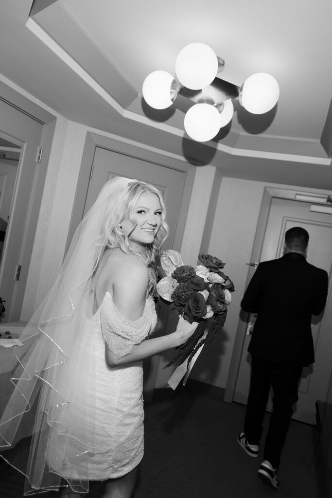 Black and white photo of the bride looking back while holding her bouquet inside her hotel room at The Cosmopolitan in Las Vegas.