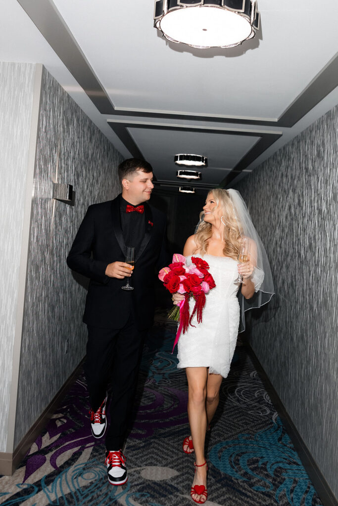 Bride and groom walk through a hotel hallway holding champagne during portraits at a Cosmopolitan wedding in Las Vegas.