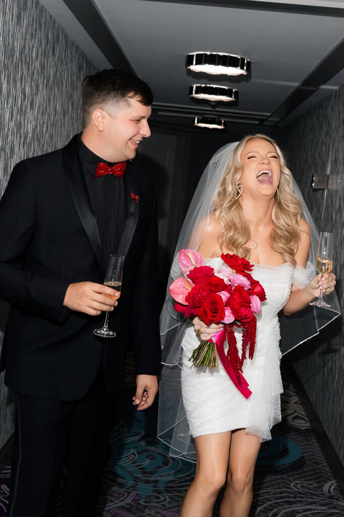 Bride laughs while holding her bouquet and champagne during playful wedding portraits at The Cosmopolitan in Las Vegas.