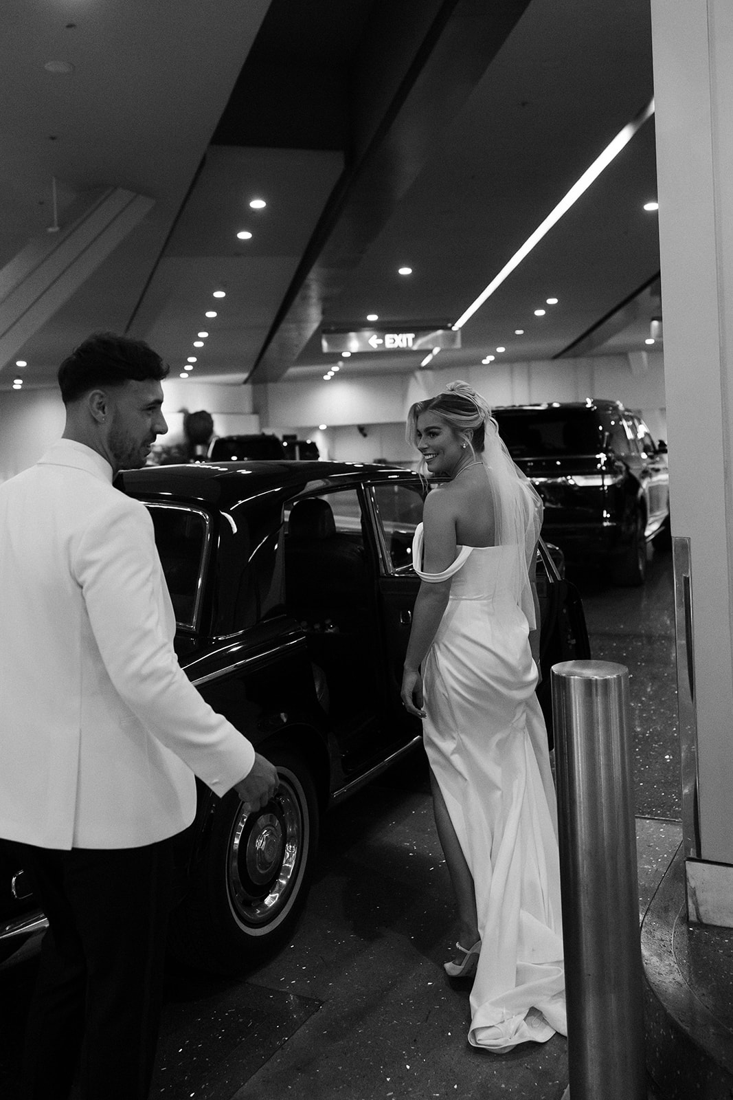 Black and white photo of a bride and groom walking to their vintage Rolls Royce in the parking garage. 