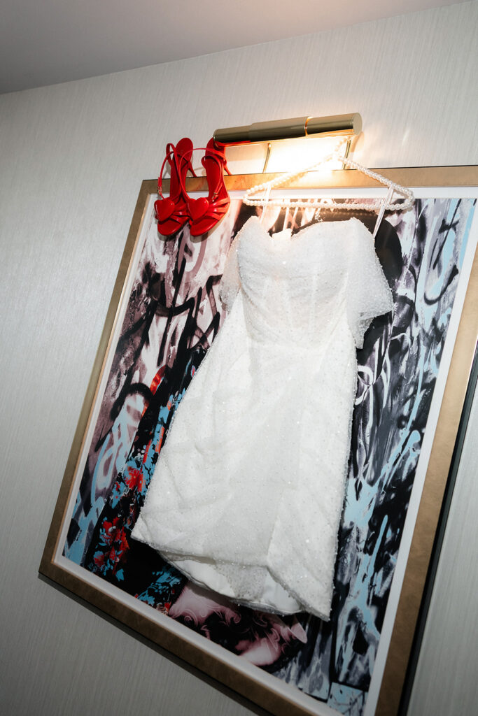 Short wedding dress hanging with red heels above it inside a suite at The Cosmopolitan in Las Vegas.