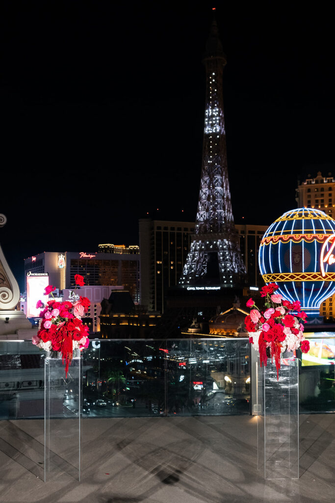 Wide view of the Boulevard Pool Deck ceremony at a Cosmopolitan wedding in Las Vegas, featuring red floral arrangements and the Paris Las Vegas Eiffel Tower in the background.