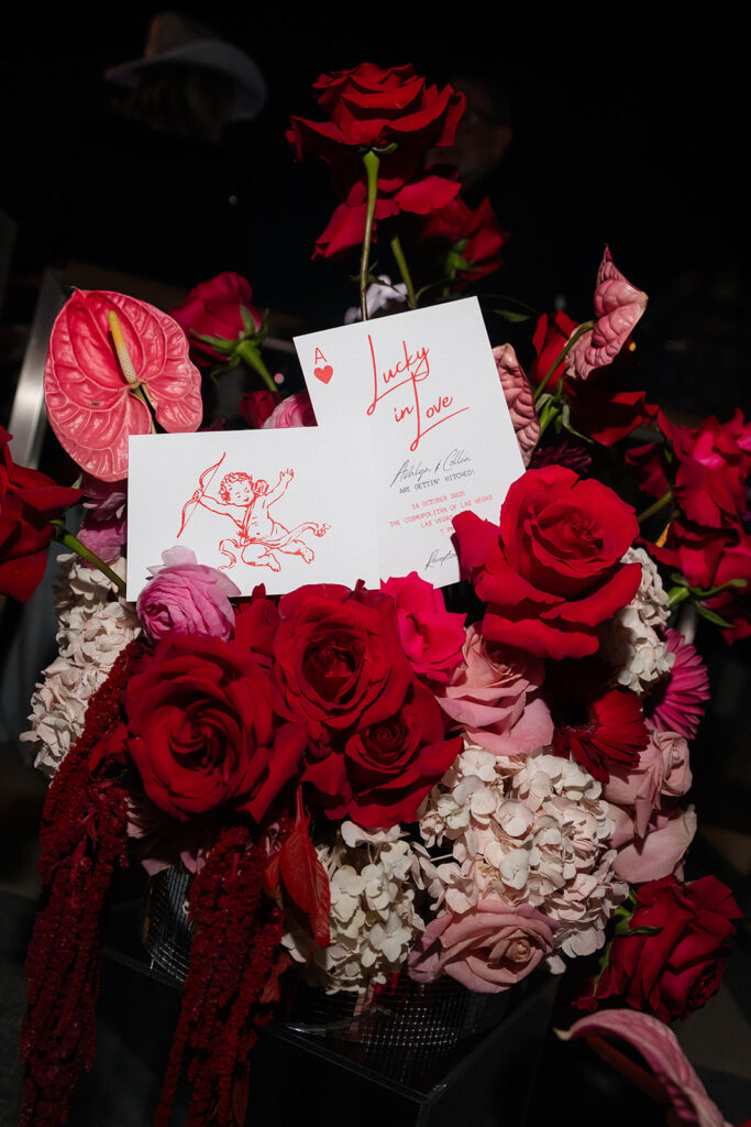 Floral arrangement with red and pink roses and custom wedding stationery.