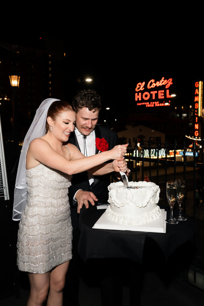 Bride and groom cutting their wedding cake on the rooftop at Commonwealth with downtown Las Vegas in the background.