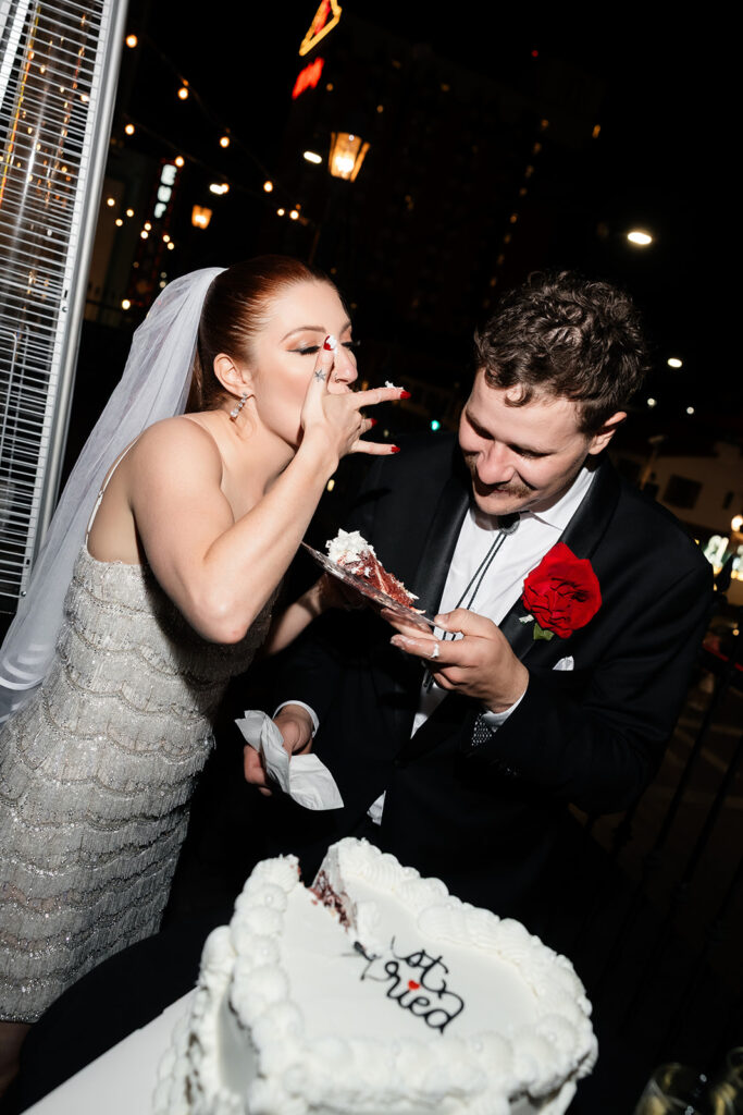 Bride playfully feeding herself cake while standing beside the groom during their Commonwealth Las Vegas wedding reception.