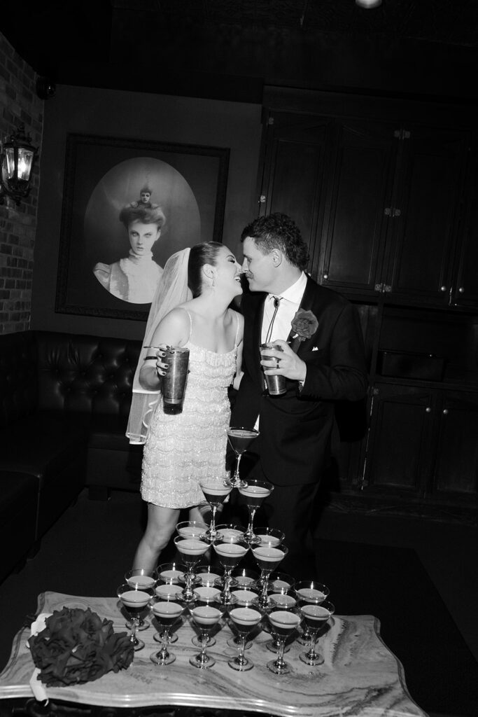 Black and white photo of the couple standing behind an espresso martini tower during their rooftop wedding reception at Commonwealth.
