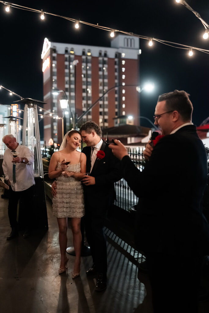 Bride and groom standing together on the rooftop at Commonwealth during their Las Vegas wedding reception as a guest gives a speech.