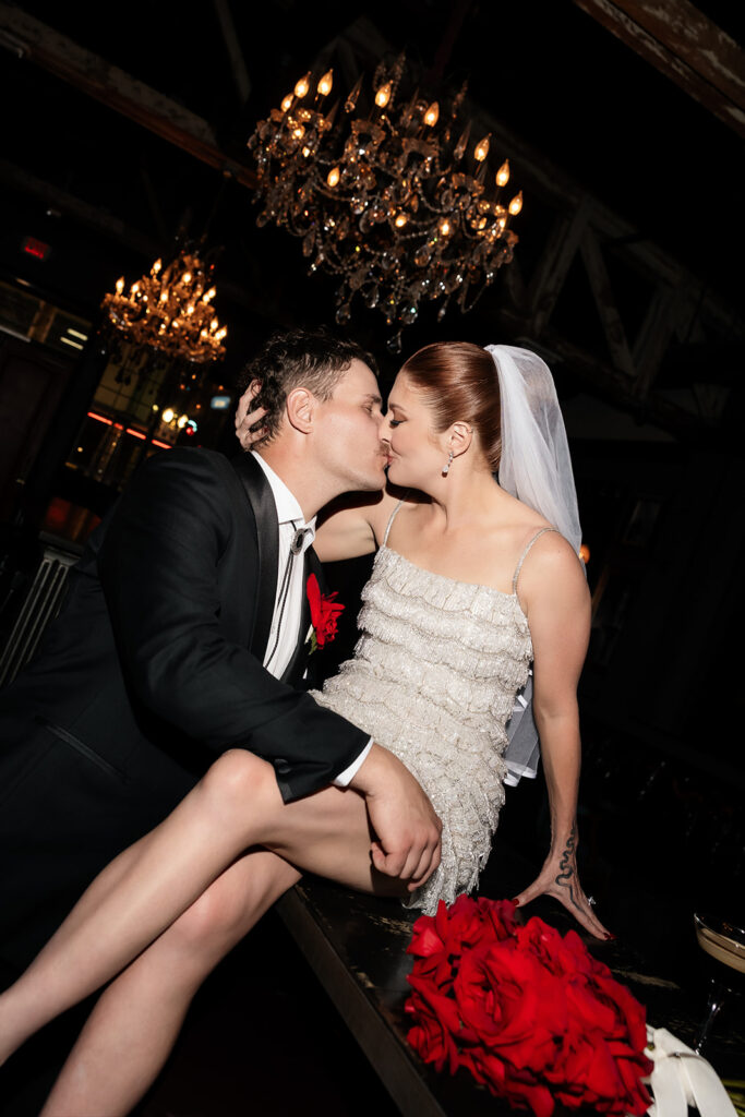 Bride and groom sharing a kiss beneath chandeliers inside Commonwealth during their wedding reception.