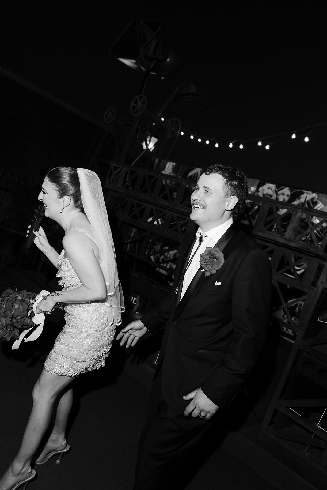 Black and white photo of the bride speaking into a microphone as the groom watches during their Commonwealth Las Vegas wedding.