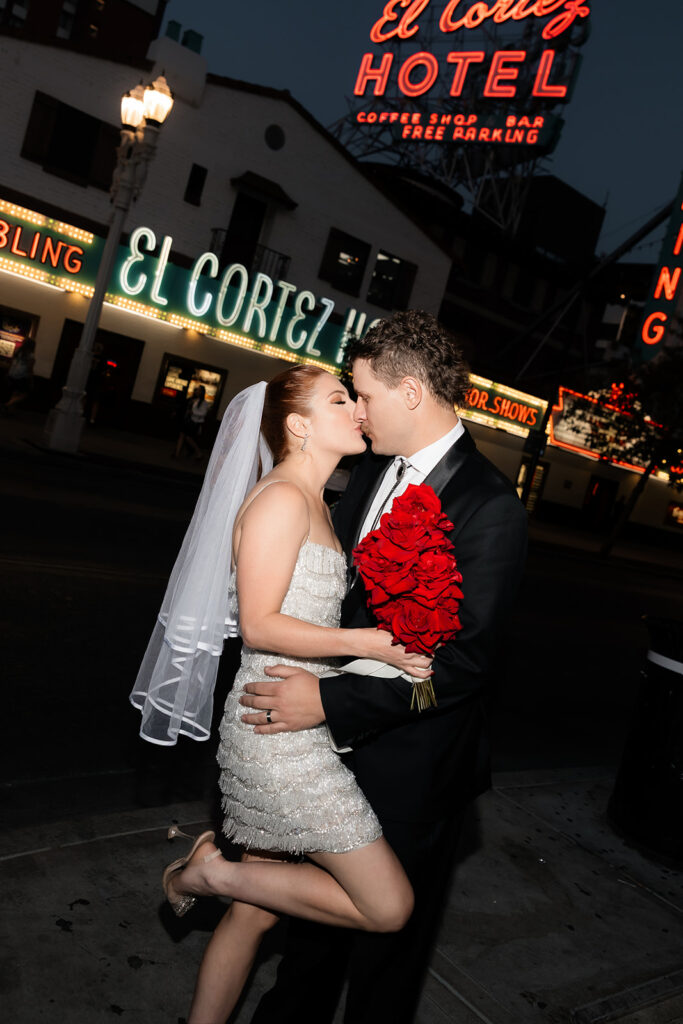Newlyweds kissing on Fremont Street in Las Vegas at night with El Cortez Hotel neon glowing behind them.