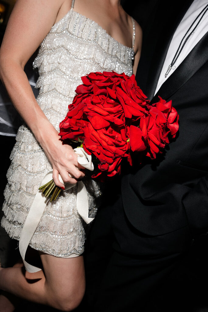 Close-up of the bride’s red rose bouquet against her beaded wedding dress during a Fremont Street Las Vegas wedding.