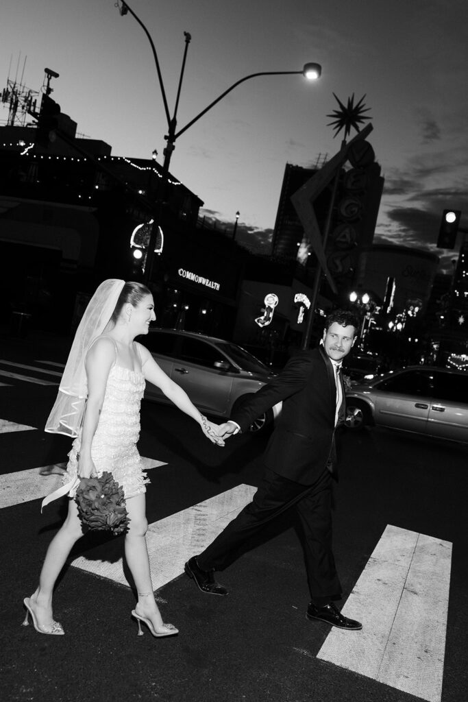 Black and white photo of a bride and groom walking across the street on Fremont during their Las Vegas wedding photos.
