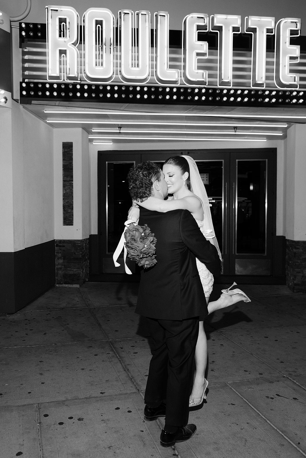 Bride and groom posing beneath the Roulette neon sign outside Commonwealth during their Las Vegas wedding reception.