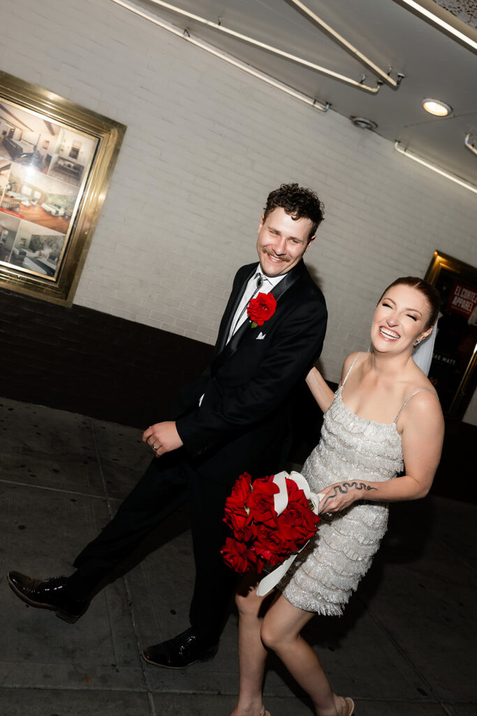 Bride and groom laughing together as they walk down Fremont Street arm in arm.
