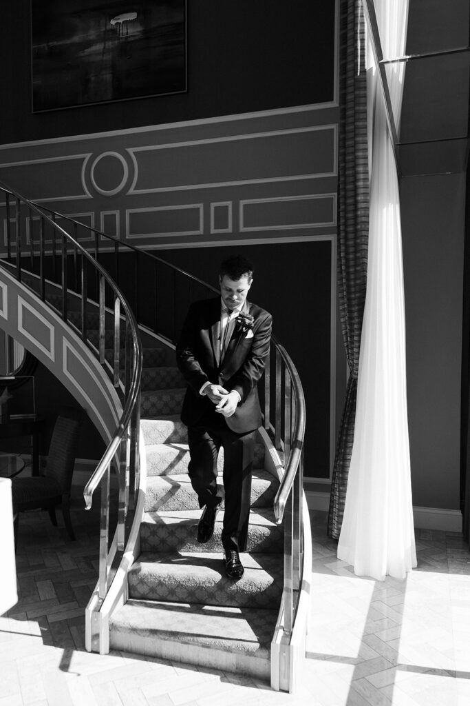 Black and white photo of a groom walking down the staircase inside the Golden Nugget.