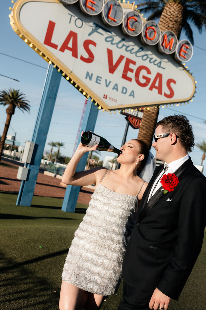 Bride and groom drinking champagne in front of the Welcome to Fabulous Las Vegas sign.