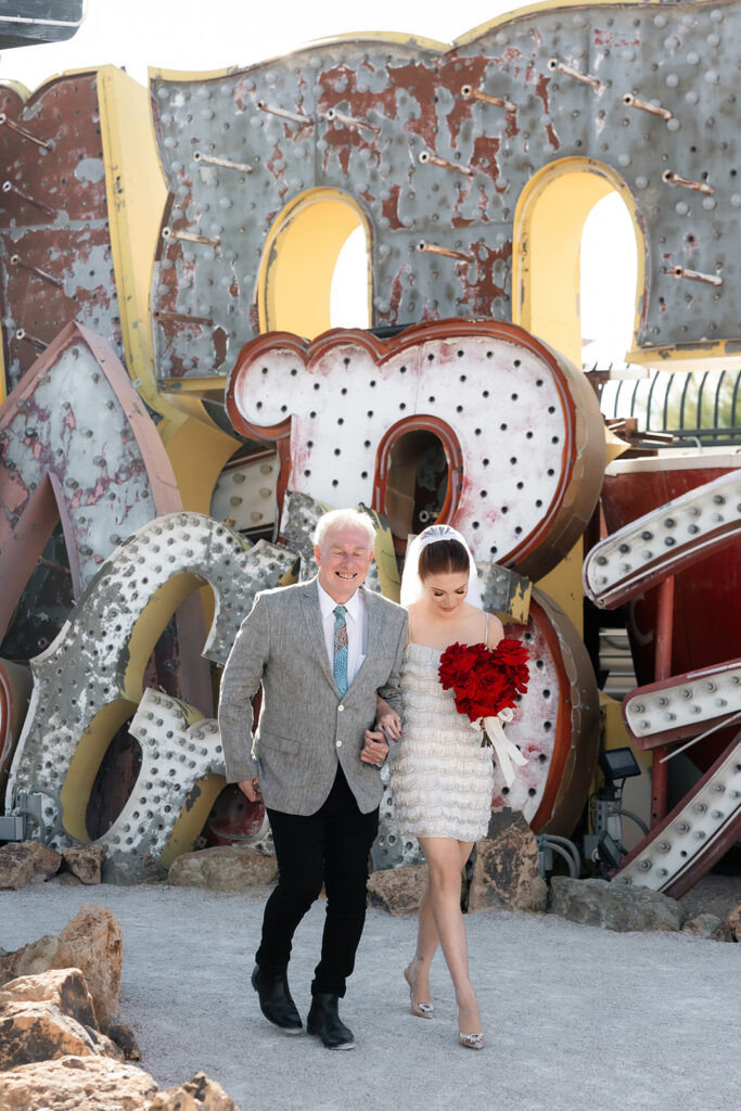 Bride walking arm in arm with a family member through the Neon Museum during a Las Vegas wedding ceremony.