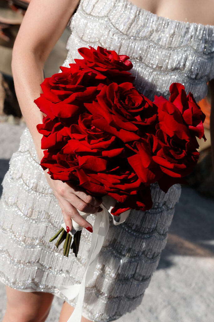 Close-up of a bride holding a bold red rose bouquet against a beaded wedding dress in Las Vegas.