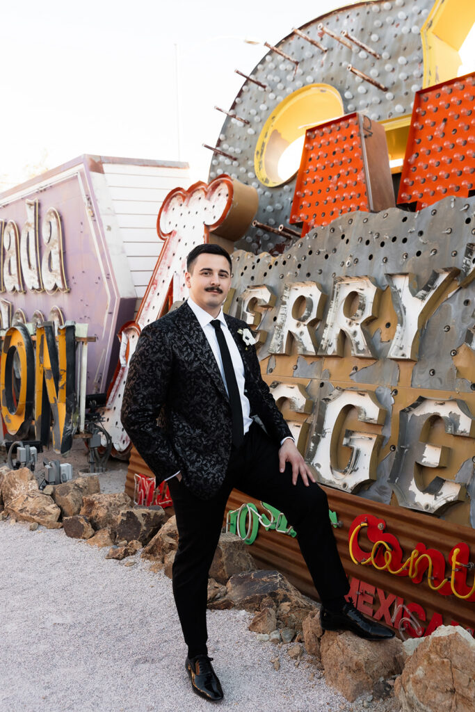 Groom posing in a patterned black suit during Neon Museum Las Vegas wedding portraits.