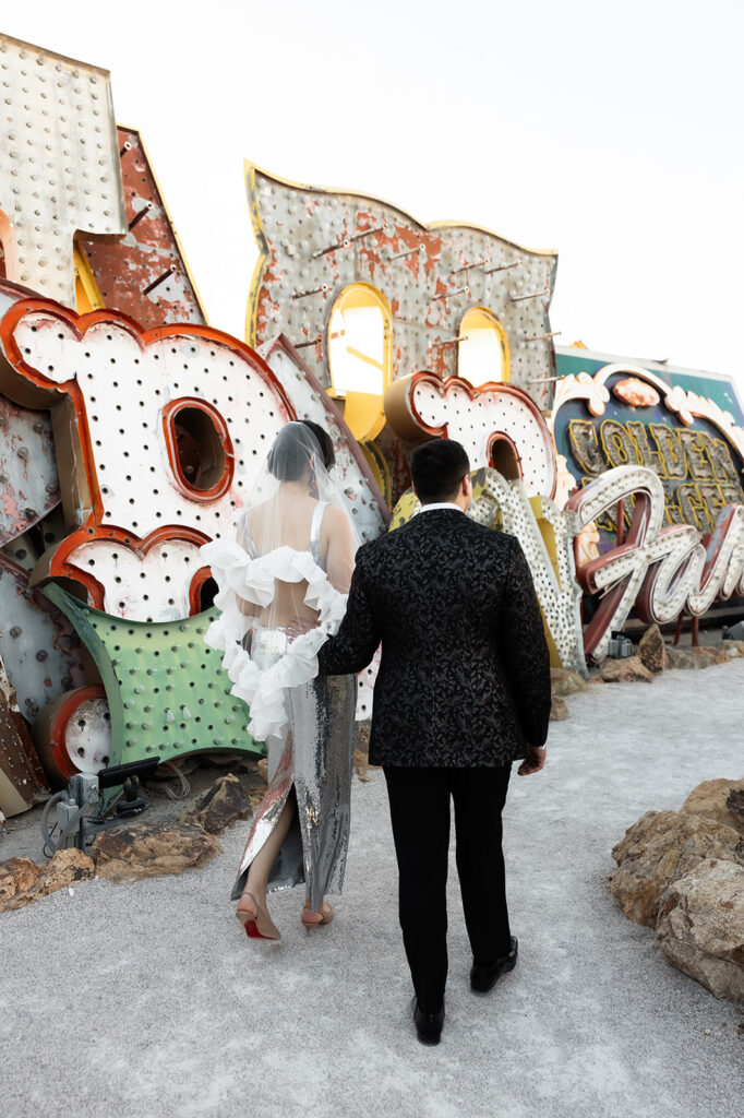 Bride and groom walking together through the Neon Museum sign collection during their Las Vegas wedding.