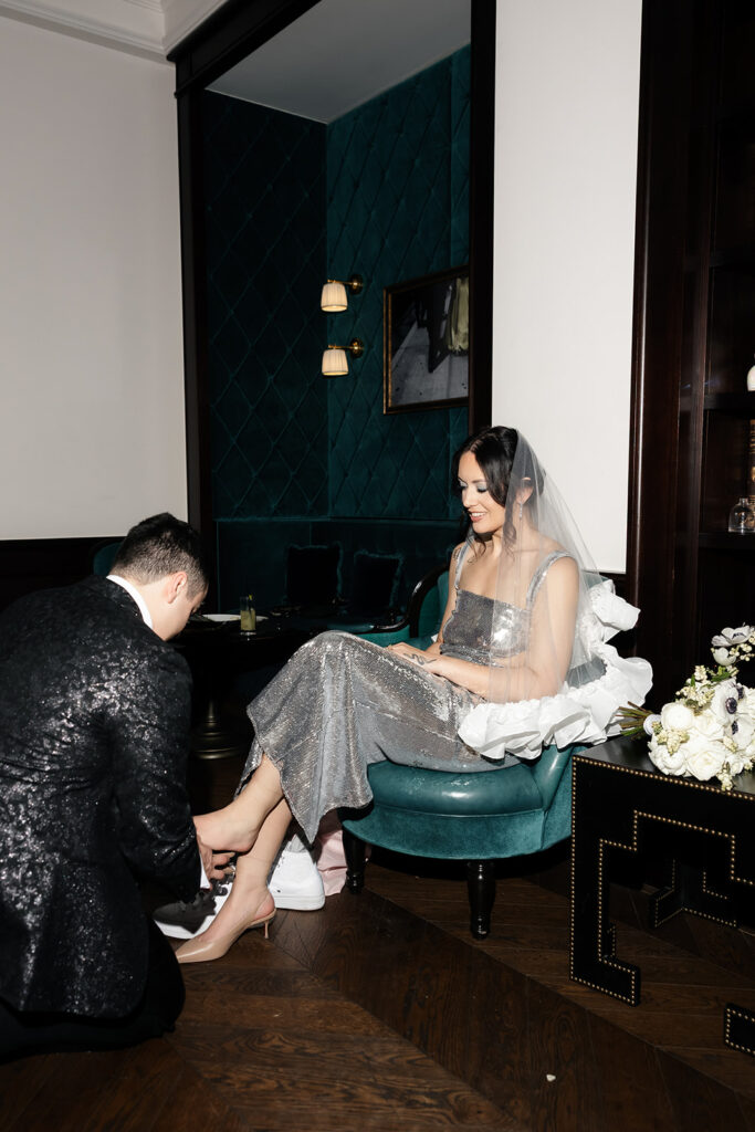 Bride sitting on a velvet chair while getting ready to change shoes during her NoMad Las Vegas micro wedding reception.