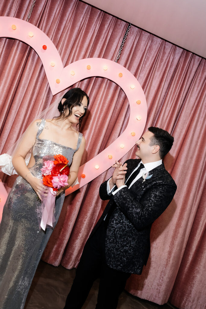 Couples candid photo in front of the heart-shaped backdrop during their Las Vegas micro wedding at Sure Thing Chapel.
