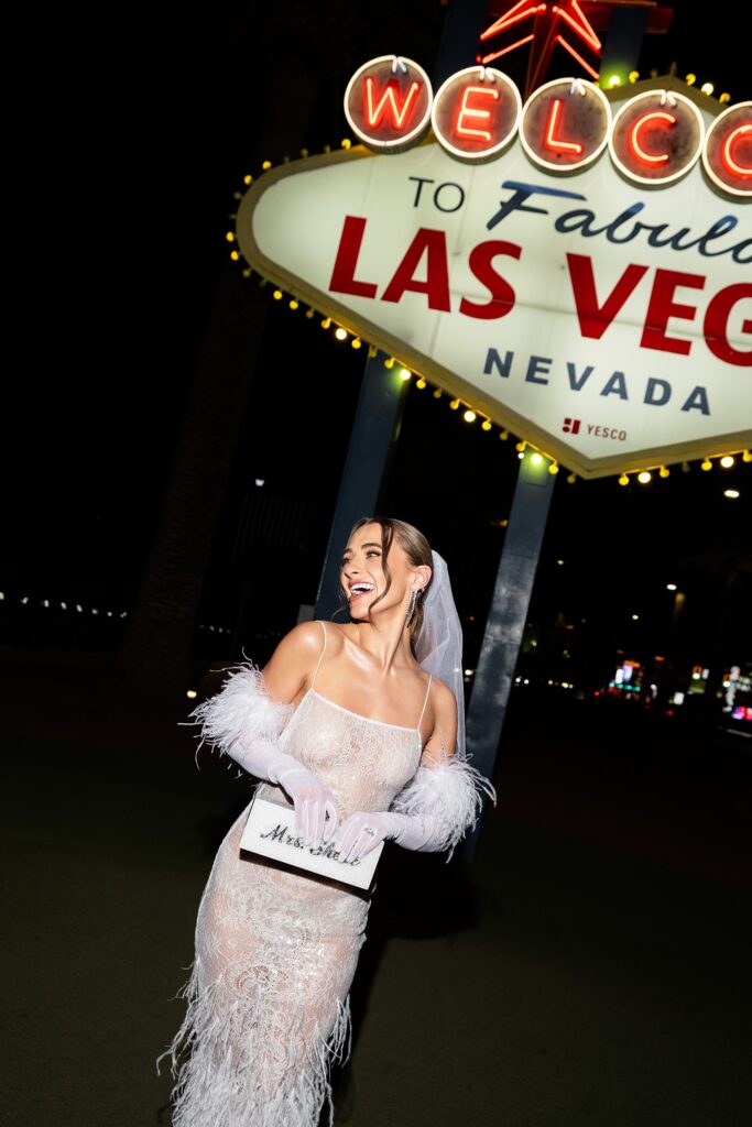 Bride smiling and posing in front of the Welcome to Fabulous Las Vegas sign at night.