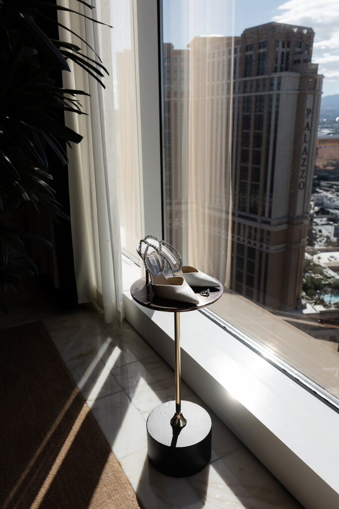 Brides rings and Jimmy Choo wedding heels sitting on a table in front of the window at Wynn Las Vegas.