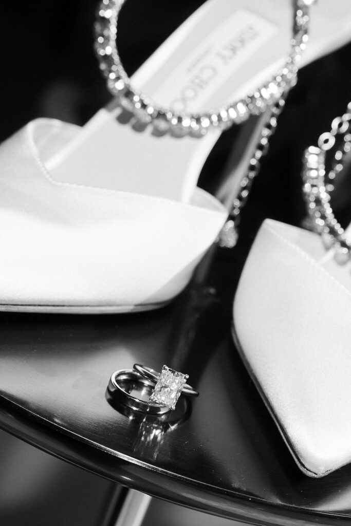 Black and white close up shot of the brides wedding rings styled next to her Jimmy Choo heels.